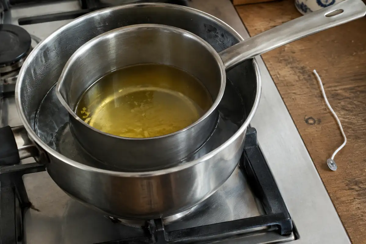 Casserole de cire fondue au bain-marie avec une mèche en coton posée à côté