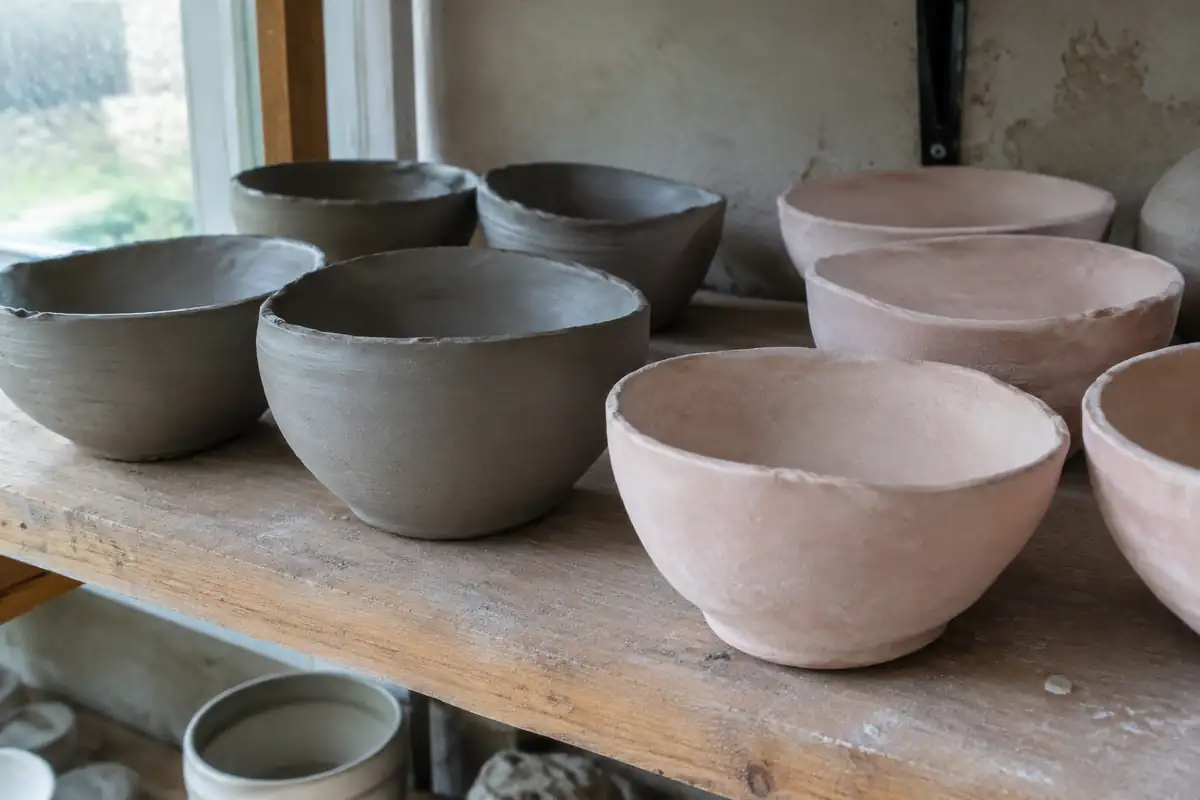 Étagère d'atelier avec des bols crus gris à côté de bols biscuités rosés
