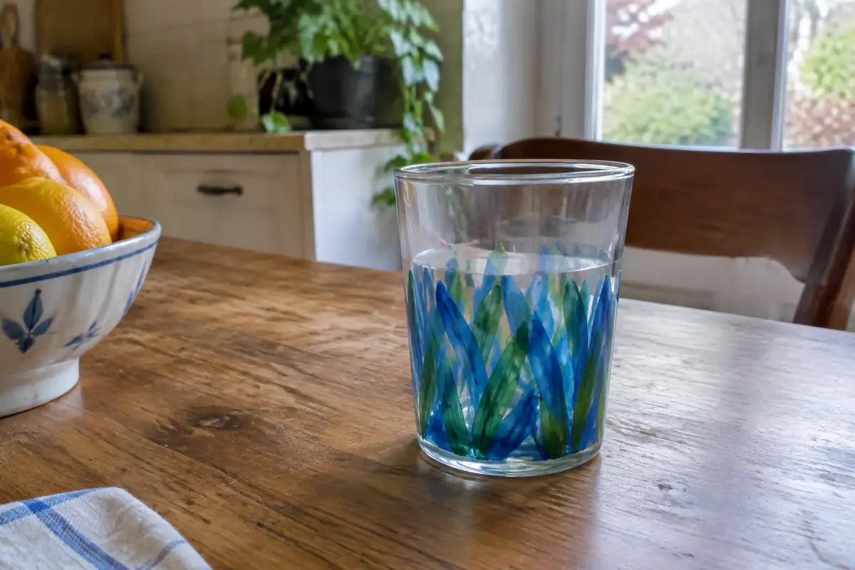 Verre à boire peint de motifs bleus et verts sur sa partie basse, avec une bande de verre nu sous le bord